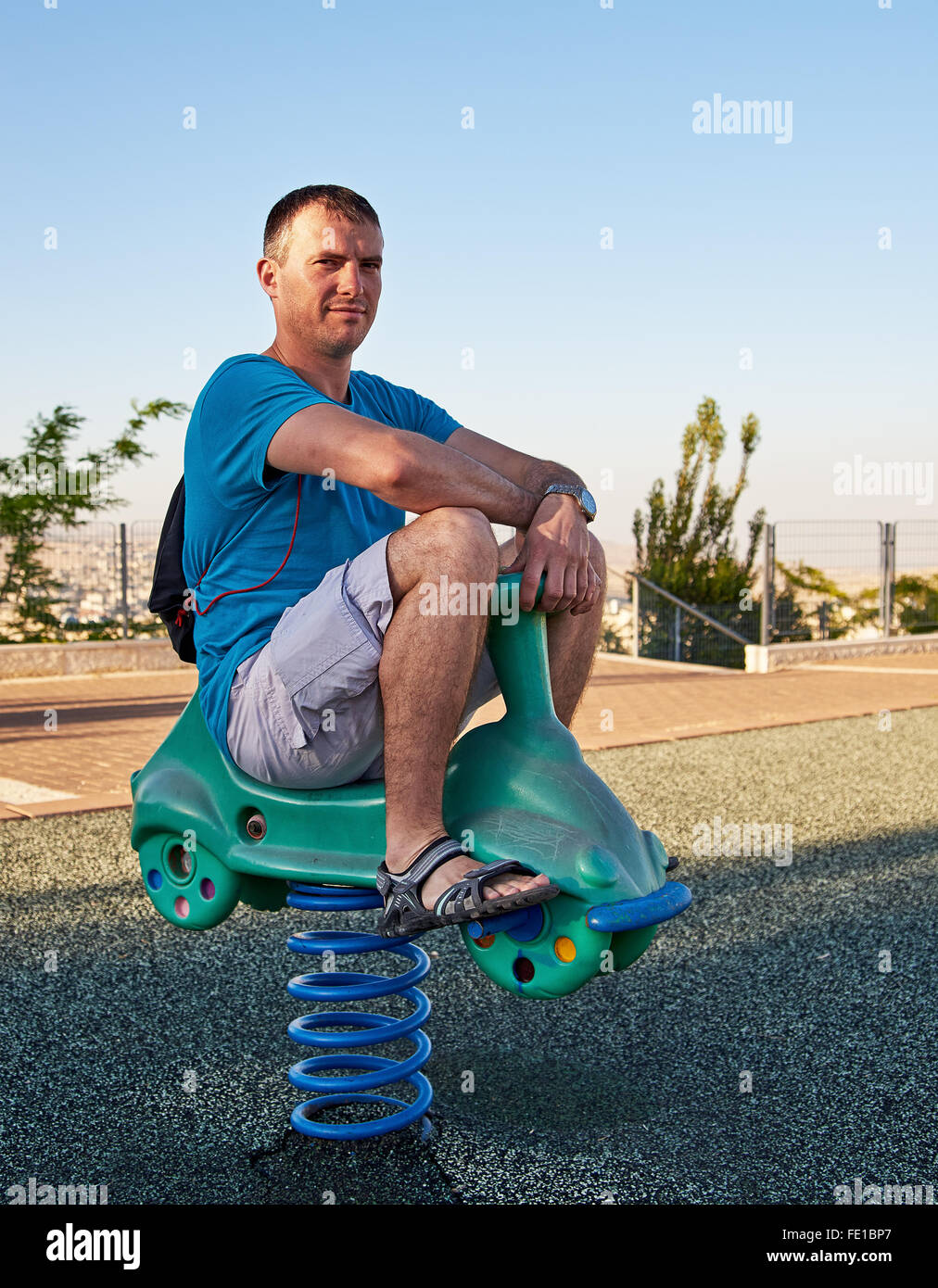 Adulto Uomo bello rivivere l'infanzia giocando in un parco giochi per bambini Equitazione sulla sede della molla. Foto Stock