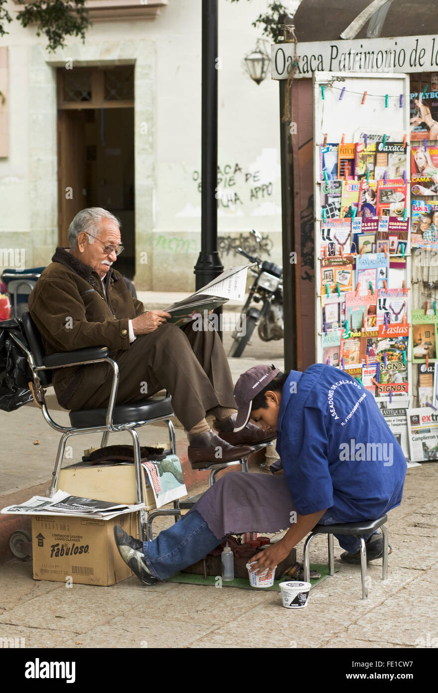 Uomo che legge il giornale mentre ottenere un lustrascarpe nella piazza centrale, la città di Oaxaca, Oaxaca, Messico. Il manuale non qualificati servizi di manodopera di classe superiore. Foto Stock