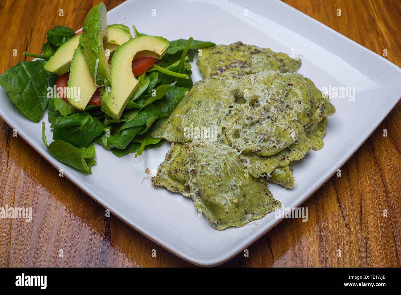 Ravioli di spinaci con salsa al pesto su una piastra con un avocado e insalata di pomodoro Foto Stock