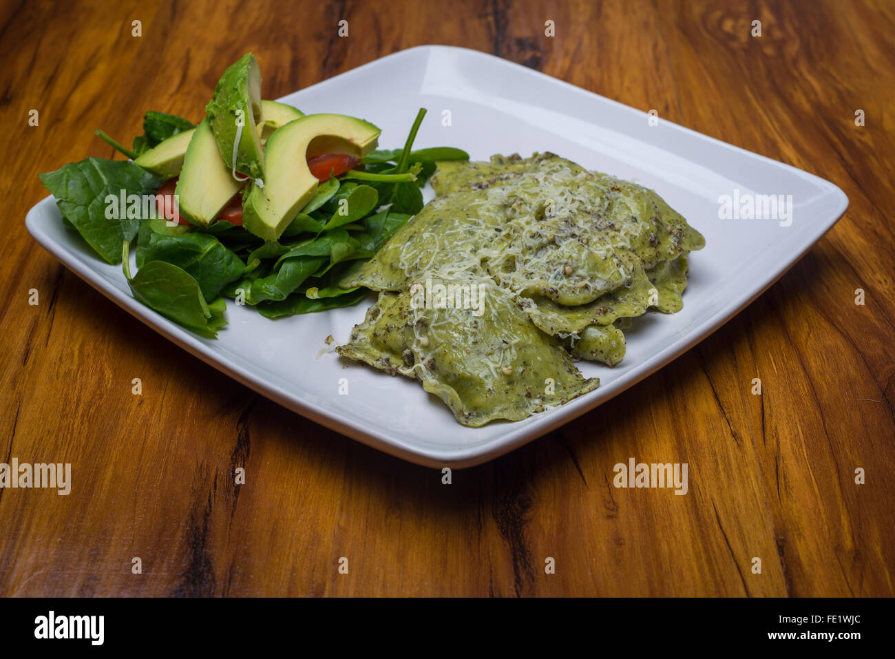 Ravioli di spinaci con salsa al pesto su una piastra con un avocado e insalata di pomodoro Foto Stock
