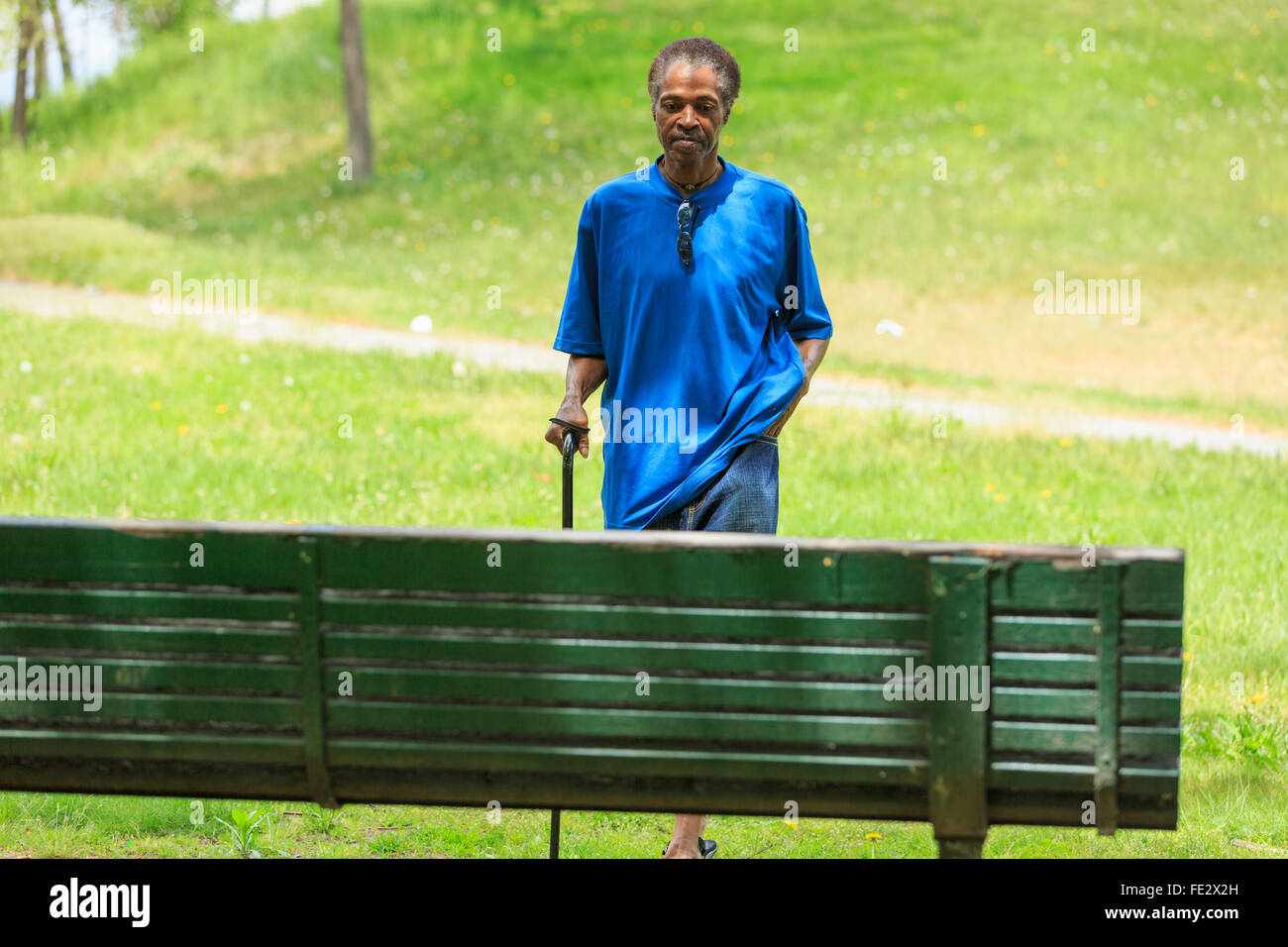 Uomo con lesione cerebrale traumatica facendo una passeggiata con la sua canna da zucchero in un parco Foto Stock