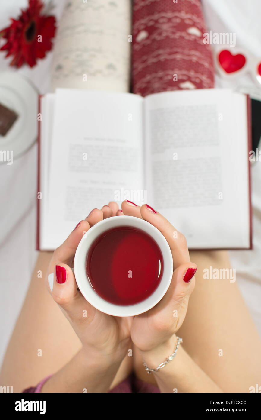 Donna con una tazza di tè nel letto e la lettura di un libro Foto Stock
