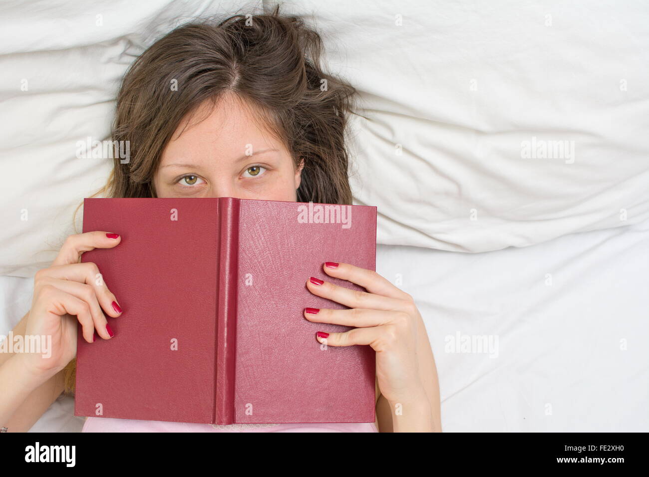 Assonnato ragazza posa in un letto con un libro nelle sue mani Foto Stock