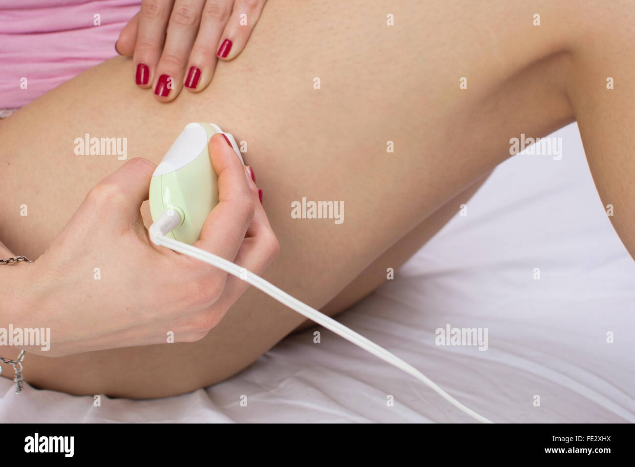 Ragazza epilates la gamba con un epilatore sul letto Foto Stock