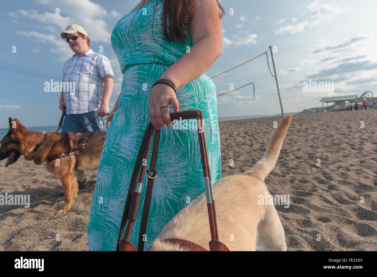 Coppia giovane con problemi visivi e cani di servizio a piedi lungo la spiaggia Foto Stock