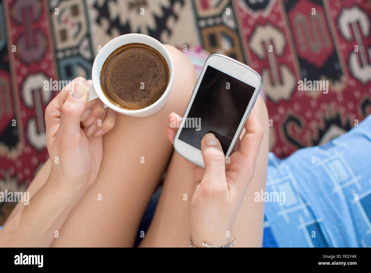 Ragazza avente il caffè a letto tenendo il suo smartphone Foto Stock