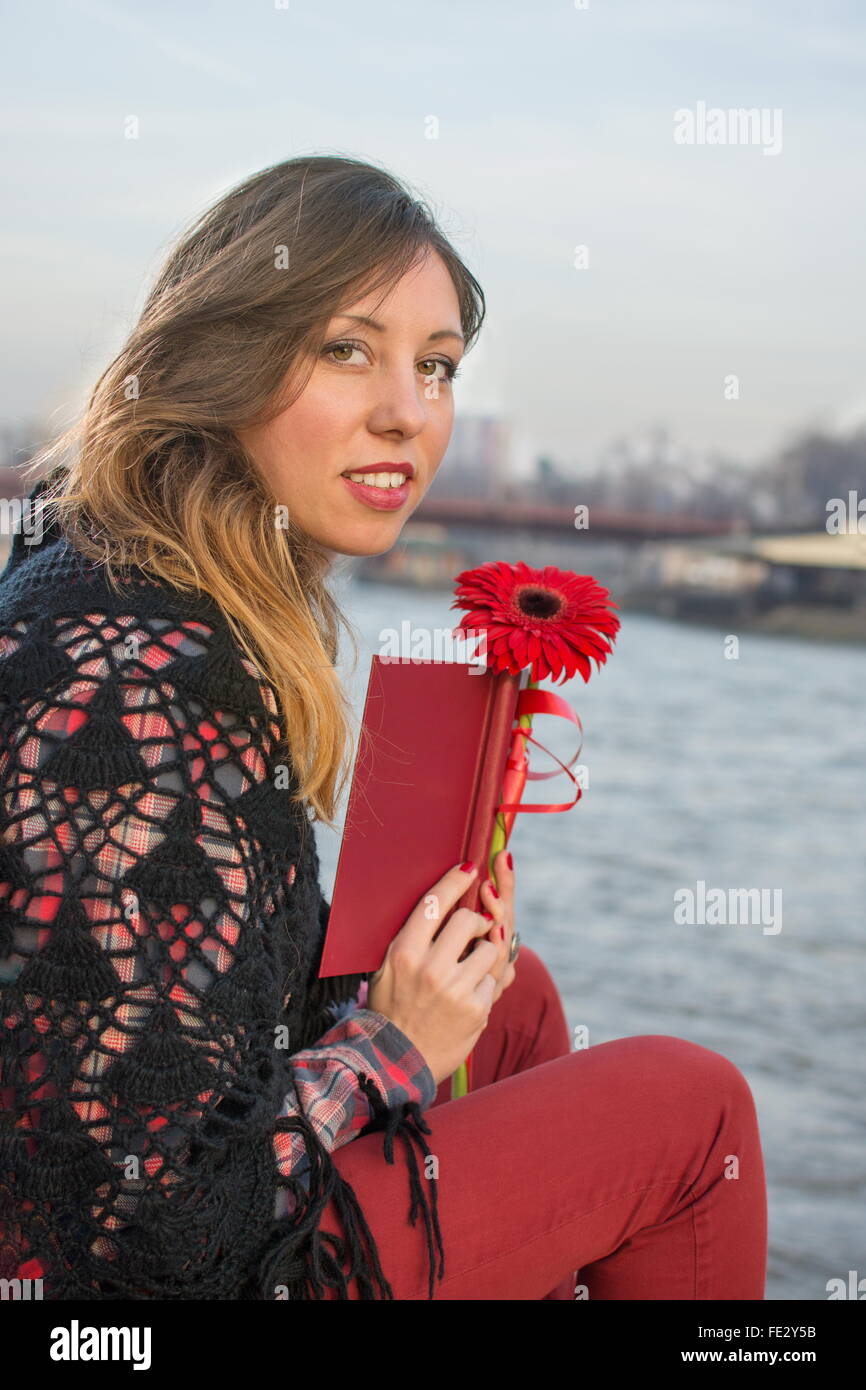 Bella bruna ragazza con un libro dal fiume bank holding fiore rosso Foto Stock