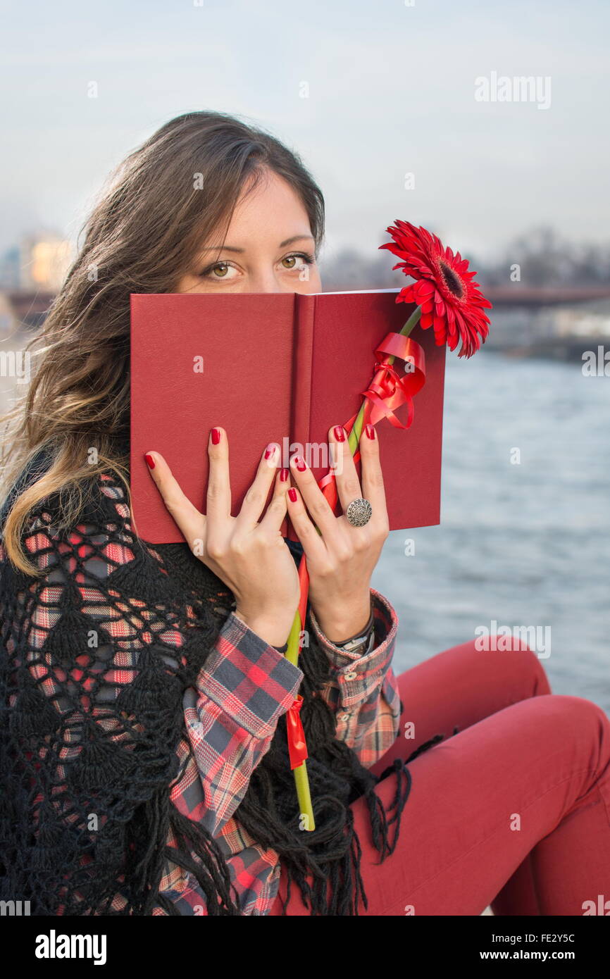 Bella bruna ragazza con un libro dal fiume bank holding fiore rosso Foto Stock