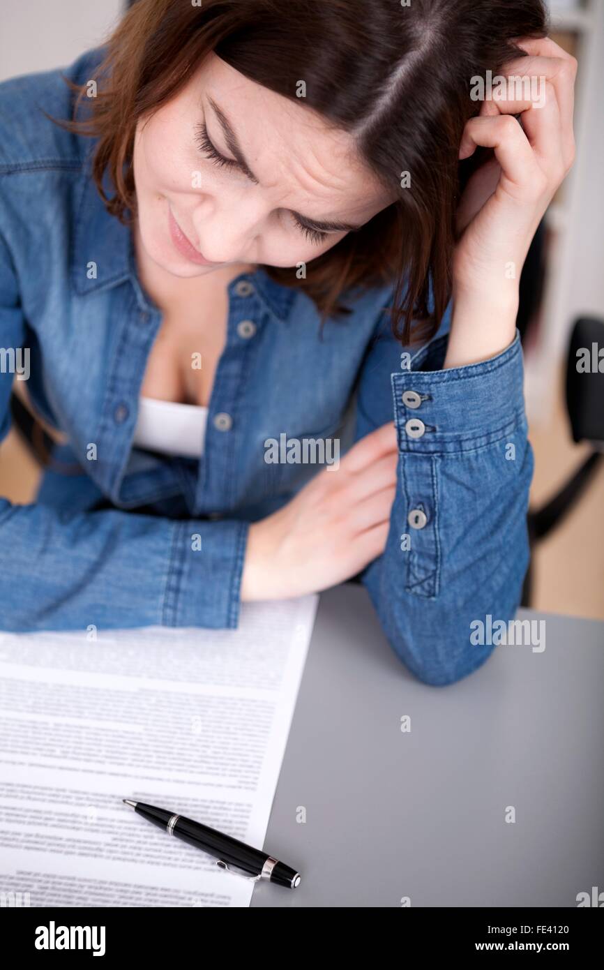 Vista ravvicinata di un attraente perplesso giovane imprenditrice con un problema seduta di graffiare la sua testa Foto Stock