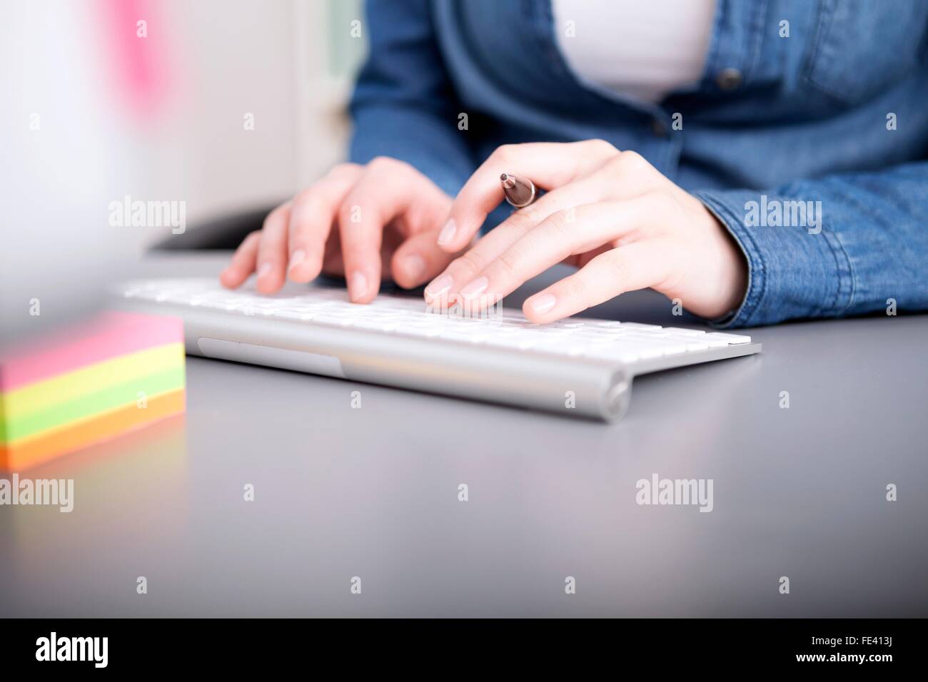 Vista ravvicinata delle mani di una imprenditrice digitazione dei dati sul suo computer su una tastiera di PC desktop Foto Stock