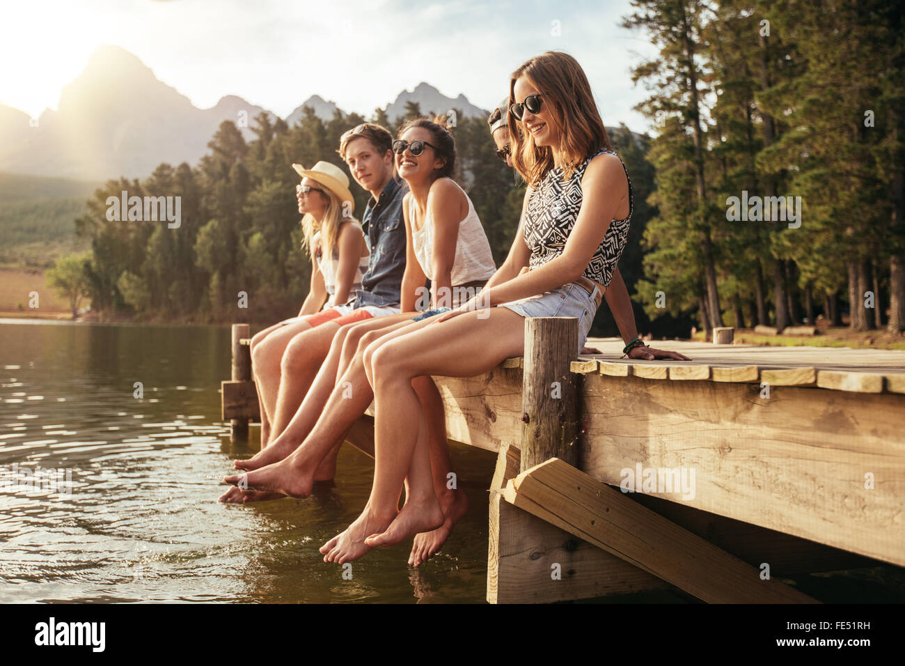 Ritratto di un gruppo di giovani seduti sul bordo di un molo, all'aperto in natura. Amici godendo una giornata al lago. Foto Stock