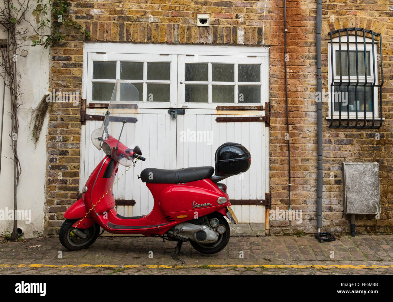 Red Piaggio scooter italiano al di fuori di un mews house vicino a Portobello Road a Londra W10 contro un bianco garage. Foto Stock