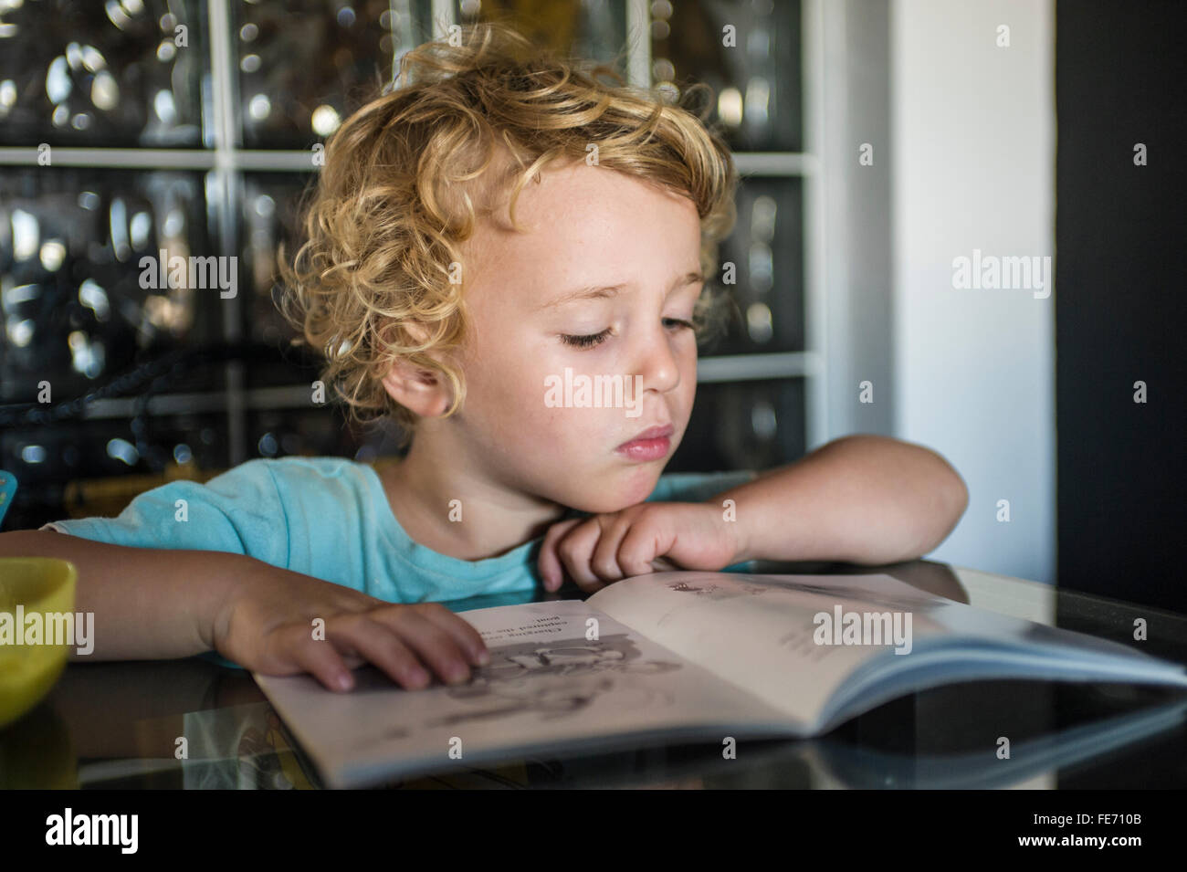 Un ragazzino (3 anni e mezzo) legge un libro a un tavolo in casa sua. Foto Stock