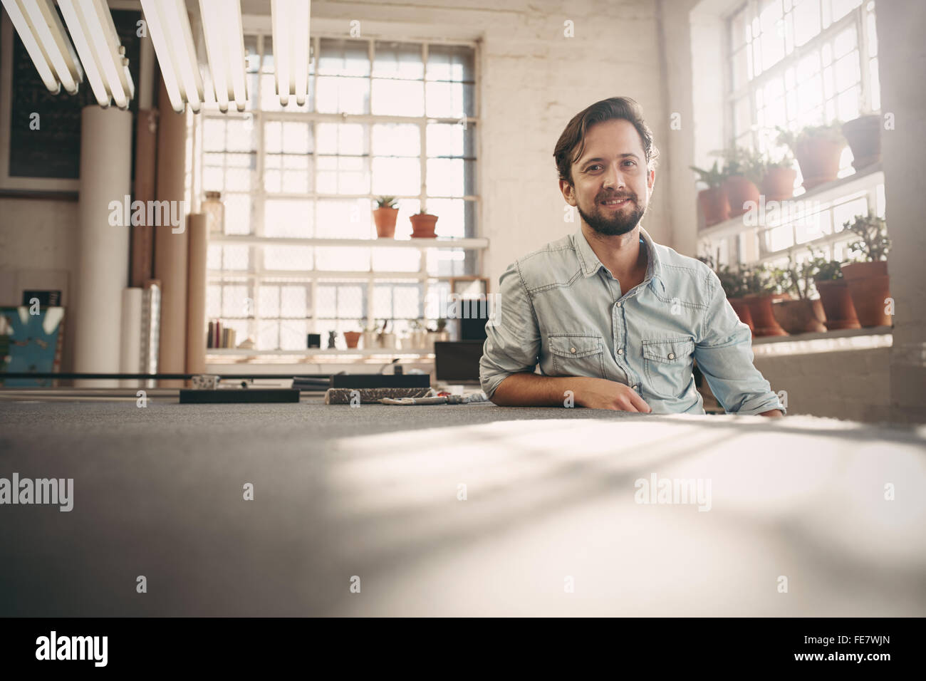 Ritratto di un proprietario di piccola impresa seduta casualmente nel suo studio worskhop guardando fiduciosi e positivo Foto Stock