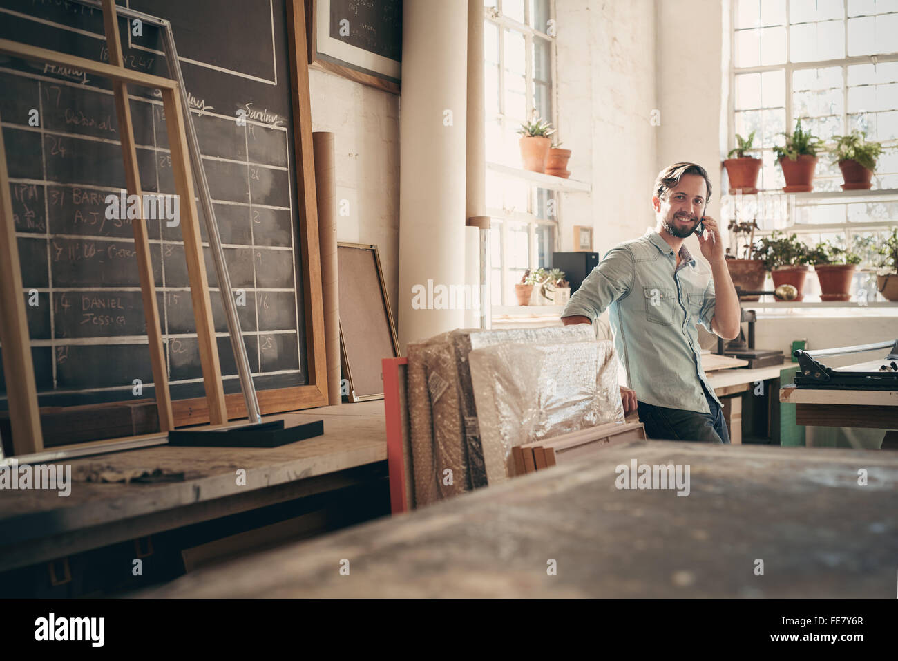 Proprietario di piccola impresa di parlare sul suo telefono cellulare mentre sorridente e in piedi casualmente nel suo studio di officina Foto Stock