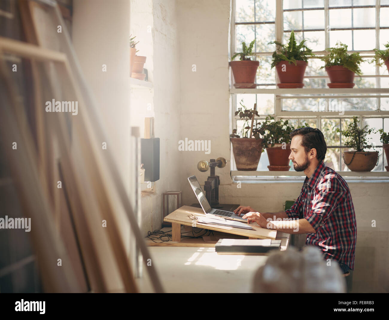 I giovani designer di sesso maschile seduto e lavorando sul suo laptop in un ufficio il suo spazio in creative design studio Foto Stock