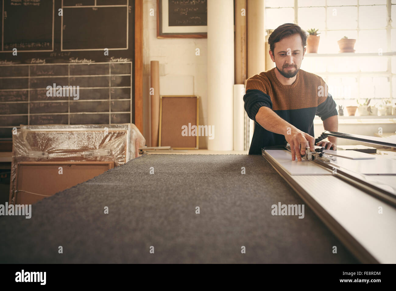 Maschi giovani designer che lavora con concentrazione e utilizzando uno strumento al suo banco di lavoro nel suo studio Foto Stock