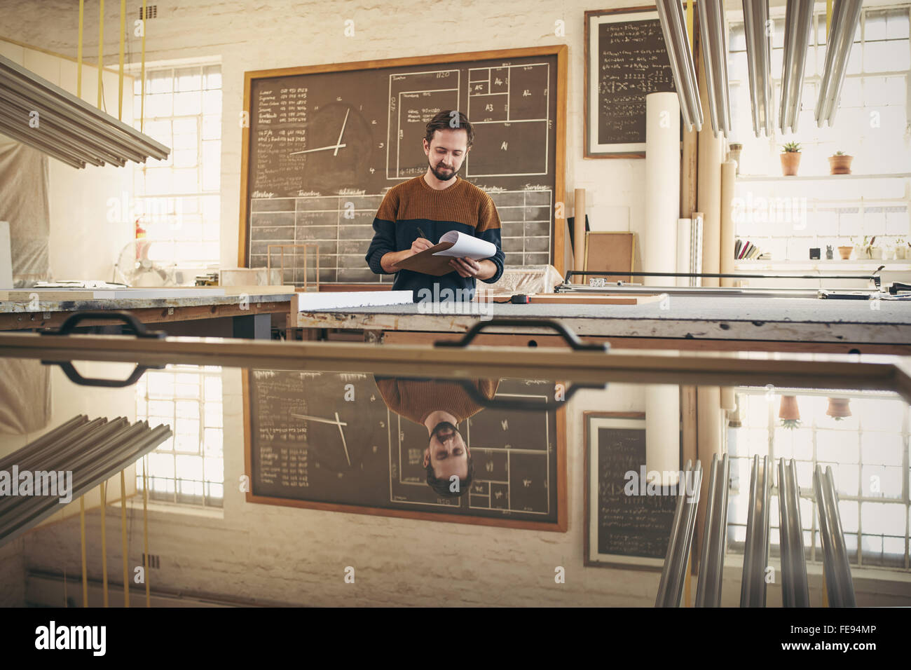 I giovani designer nel suo studio di controllo officina e magazzino gli ordini con un blocco appunti e penna Foto Stock