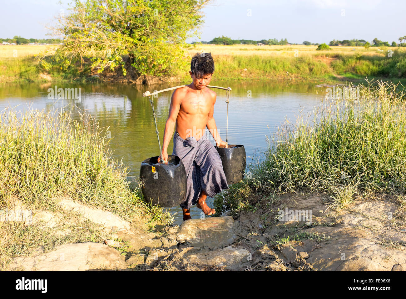 YANGON, MYANMAR - Novembre 25, 2015: Acqua portante con due secchi di ottenere acqua nella campagna dal Myanmar Foto Stock