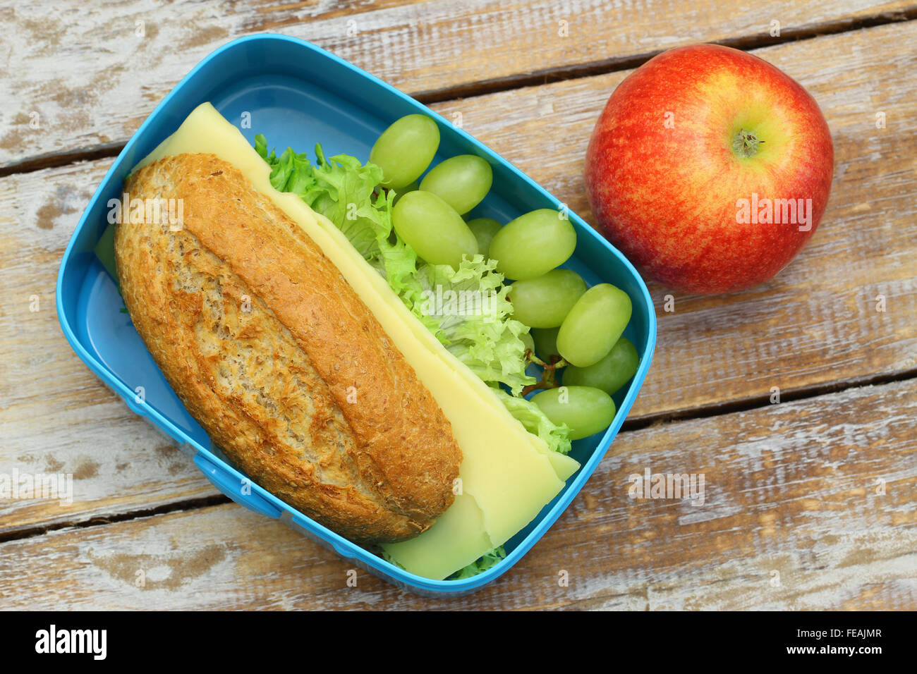 Pranzo sano scatola contenente il pane marrone sandwich di formaggio, uva e mela rossa Foto Stock