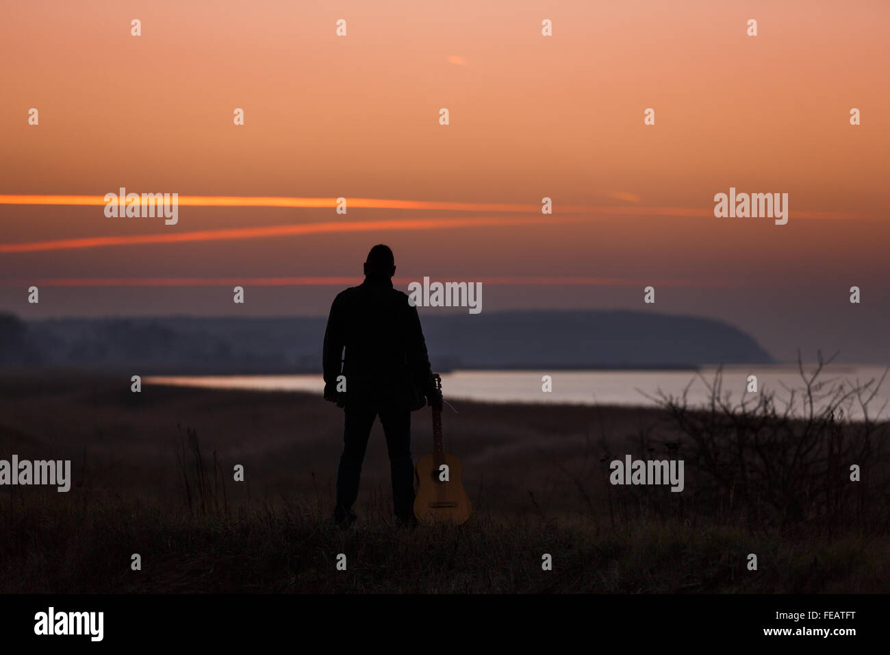 Uomo in piedi con la chitarra nel tempo al tramonto Foto Stock