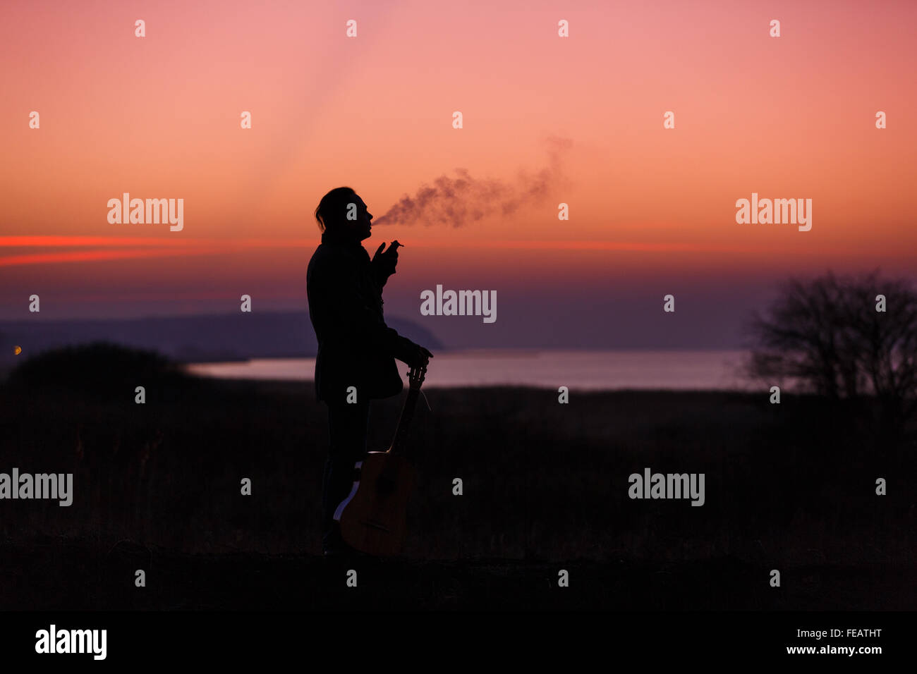 Uomo di fumare una sigaretta con la sua chitarra al tramonto Foto Stock