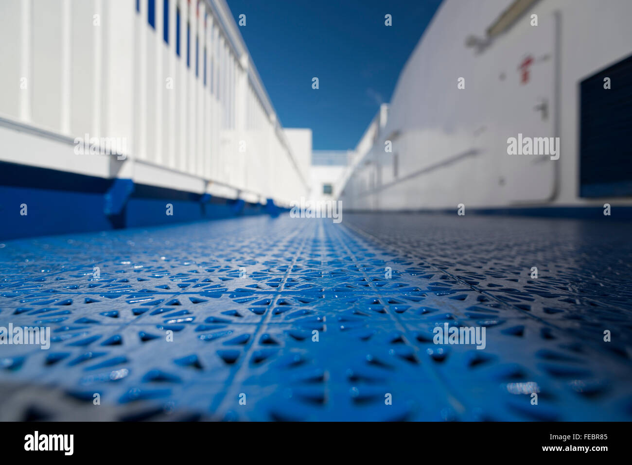 Grandangolo e close-up shot di blu tavoloni contro la ringhiera bianco e pareti sotto un cielo privo di nuvole di un ponte di una nave Foto Stock