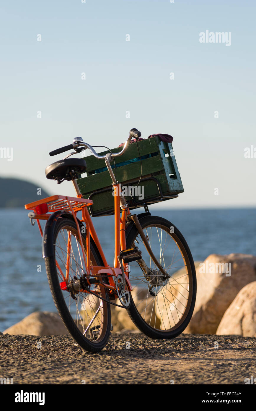 Orange vintage bicicletta con green box di trasporto in legno nella parte anteriore di mare azzurro e rocce di harbor mole,Vik,Skane,Svezia Foto Stock