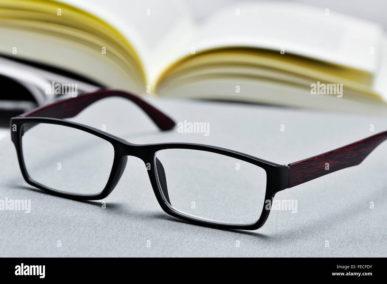 Primo piano di un paio di occhiali e un libro aperto in background Foto Stock