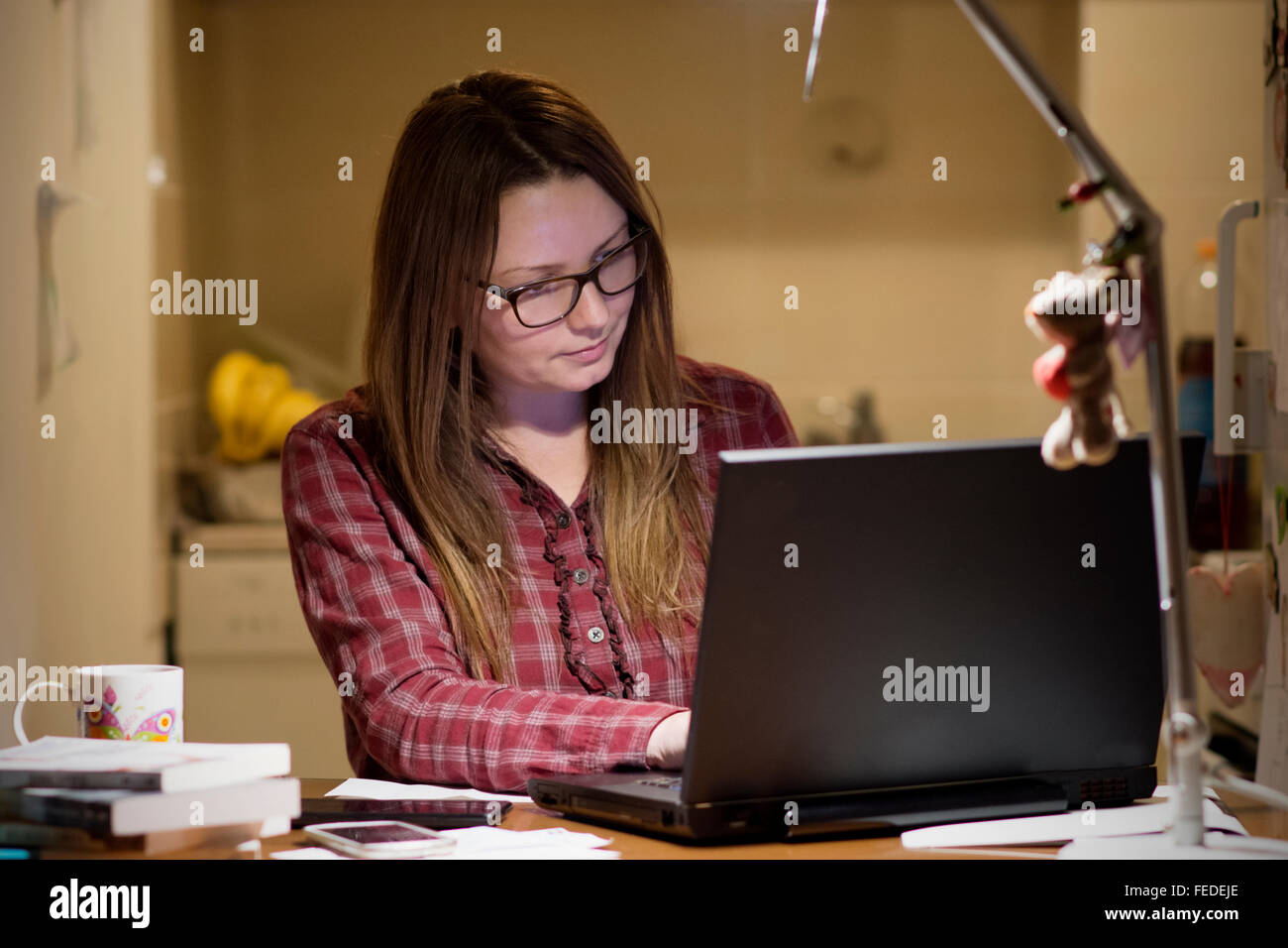 Giovane casalinga di pagare le bollette online la sera tardi dopo aver terminato tutte le sue casa di lavoro, seduto alla scrivania con computer, b Foto Stock