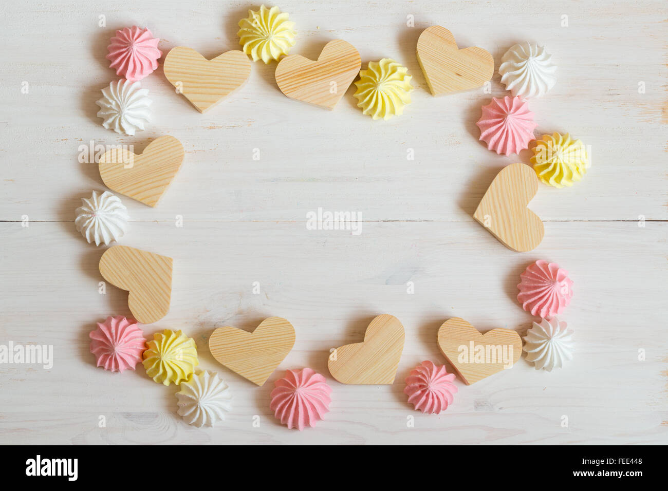 Cornice fatta di cuori di legno e meringa colori pastello su un bianco sullo sfondo di legno. Immagine del giorno di San Valentino Foto Stock