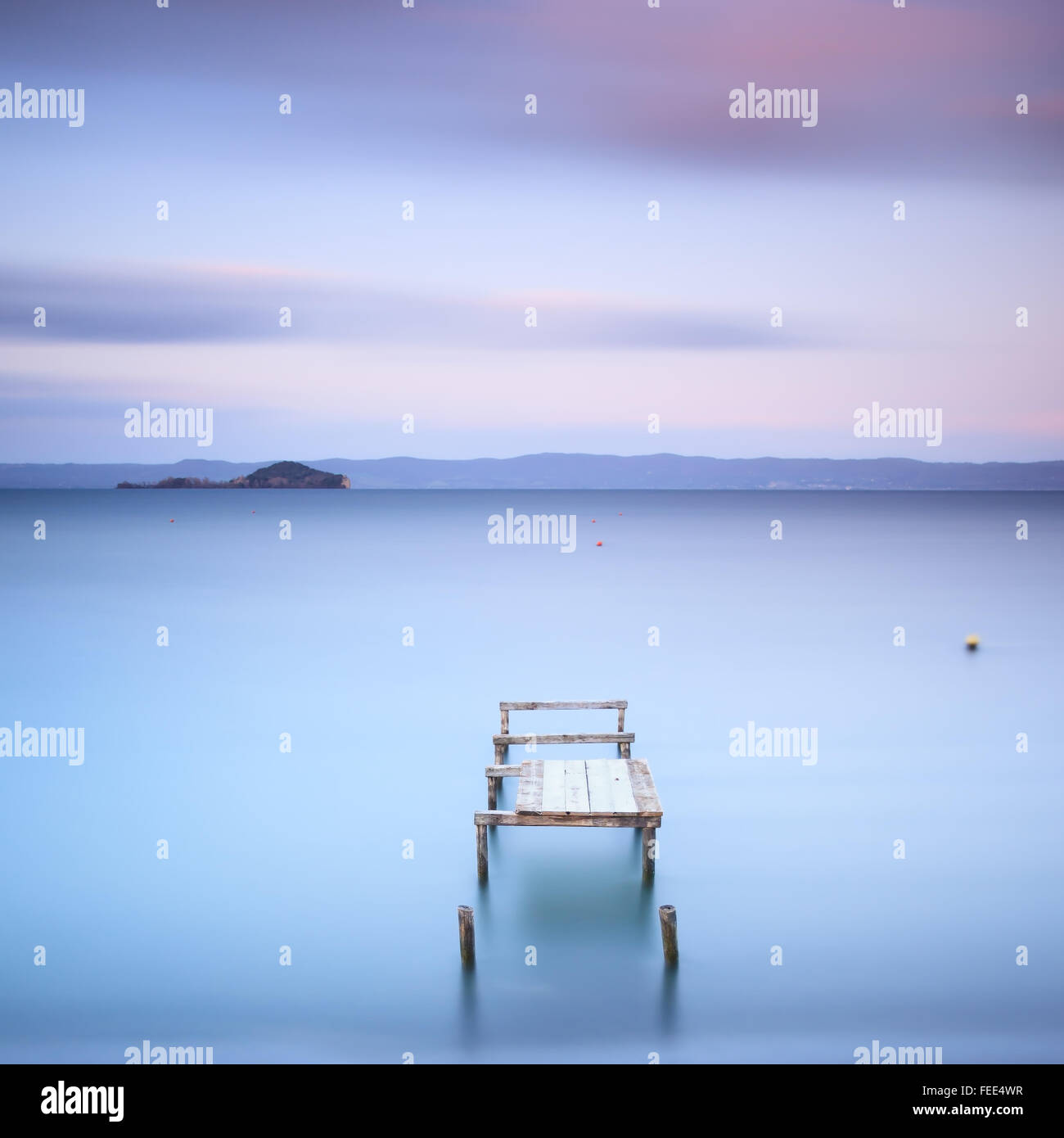 Il molo di legno o molo su un lago blu. Colline sullo sfondo. Fotografie con lunghi tempi di esposizione nel lago di Bolsena, Italia, Europa. Foto Stock