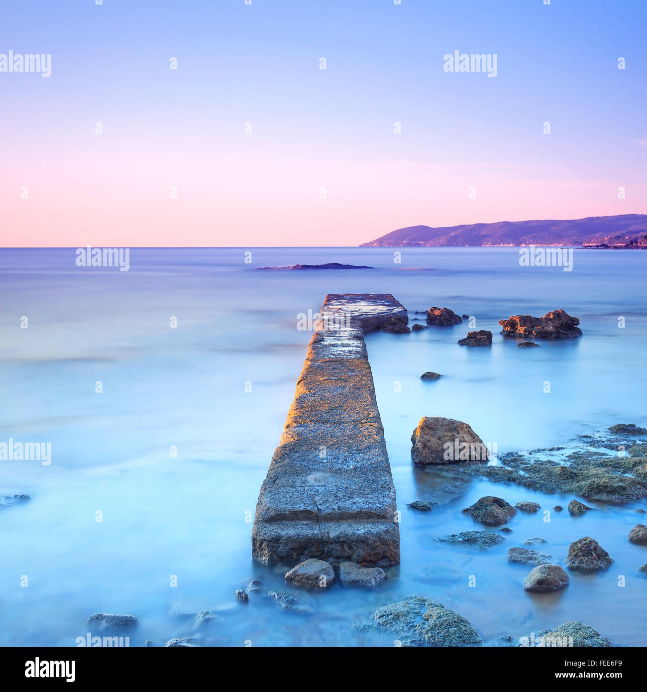 Molo di cemento o un pontile e scogli su un mare blu. Colline sullo sfondo. Fotografie con lunghi tempi di esposizione. Foto Stock