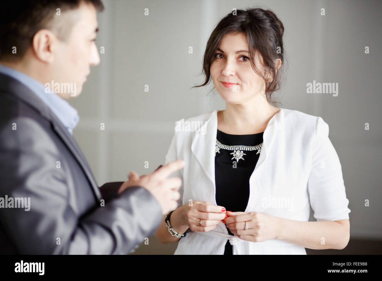 Successo attraente bruna, tipo occhi, dipendente di sesso femminile in ufficio a parlare di lavoro con il capo, durante la pausa. Indossando giacca bianca, gioielli. Carino giovane donna. Subordinazione, superiori. Foto Stock