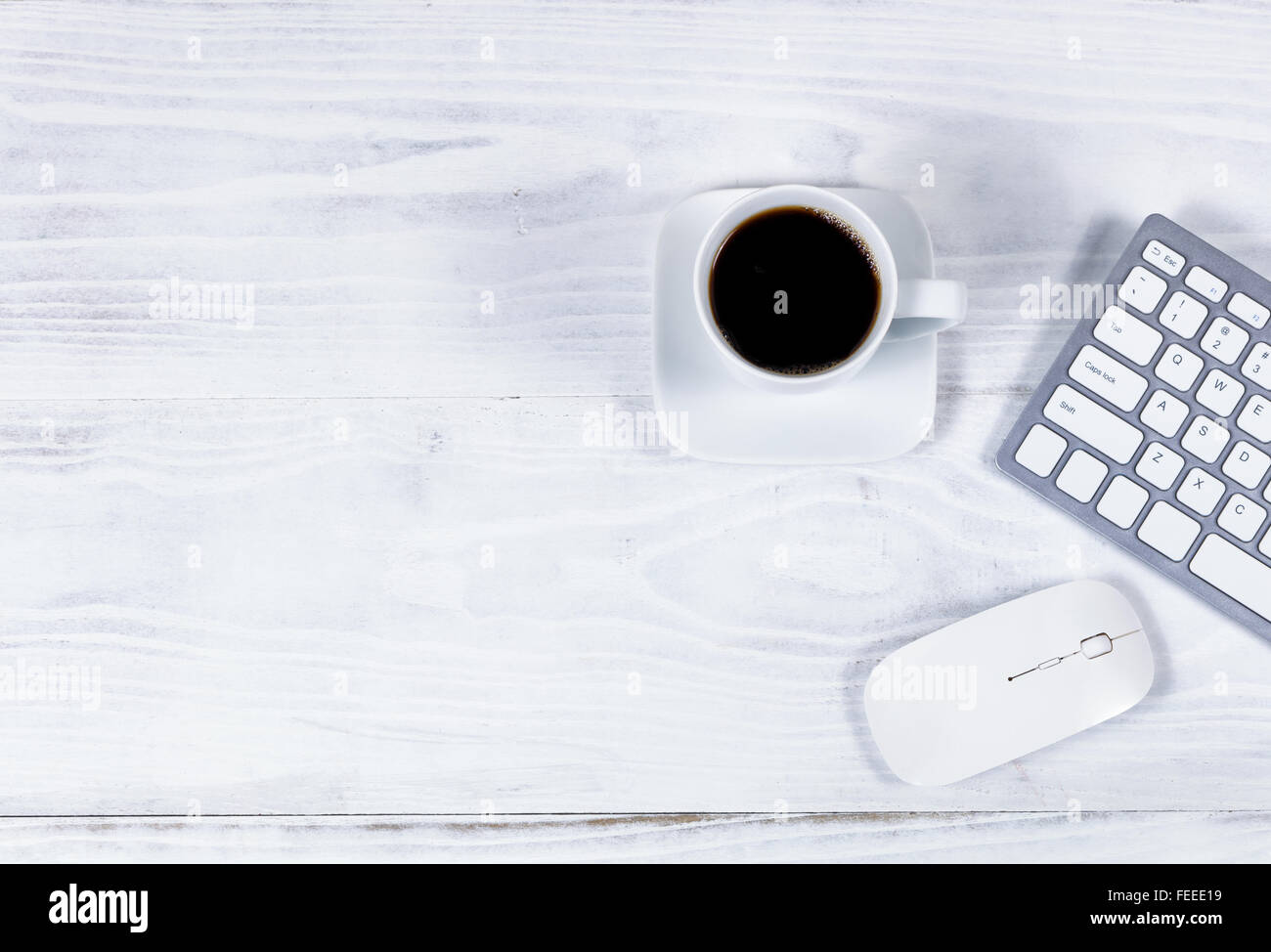 Vista aerea del desktop bianco con tastiera parziale, caffè nero e il mouse del computer. Foto Stock