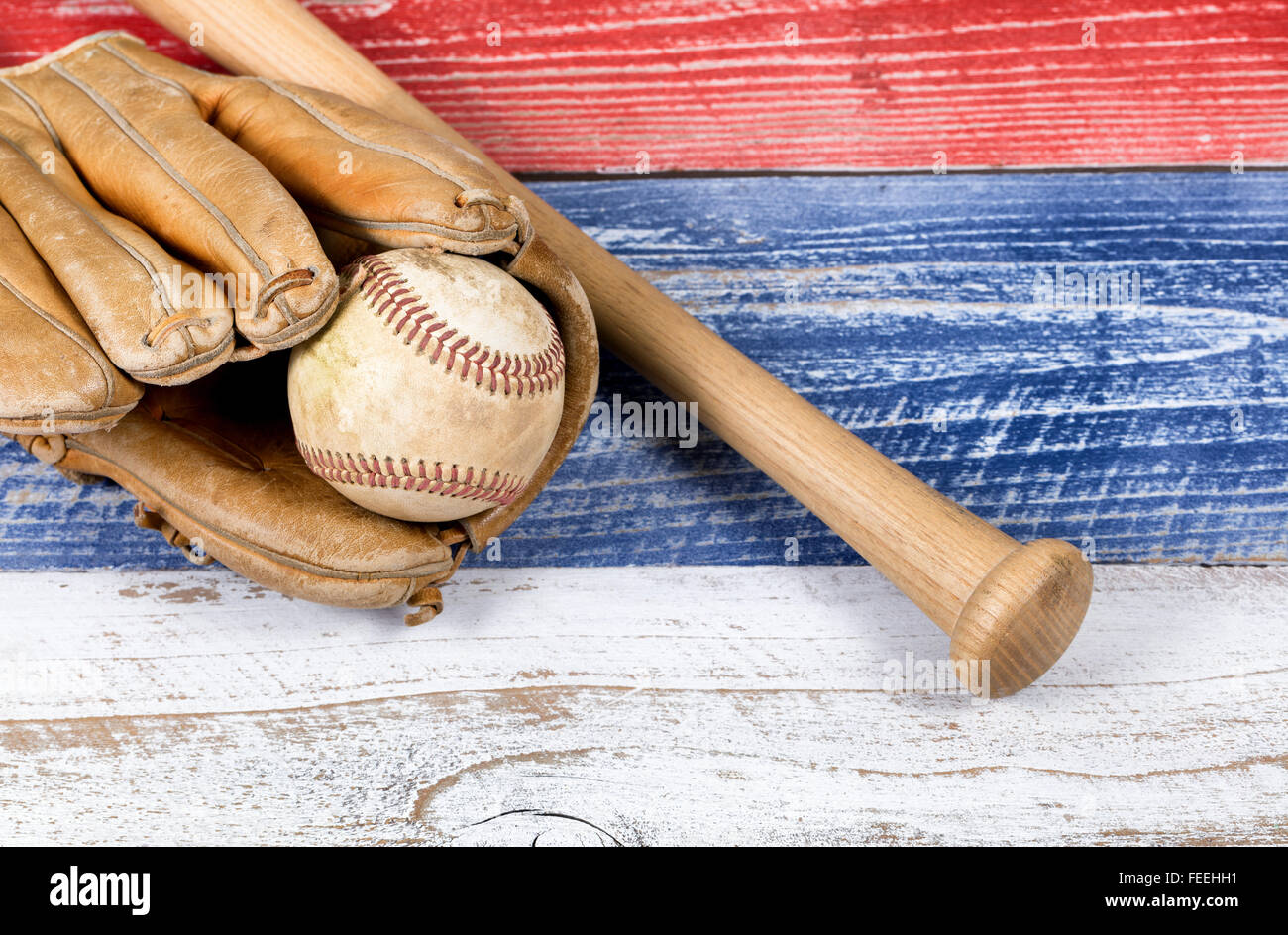 Chiusura del vecchio usurato guanto da baseball, utilizzati e di baseball bat sbiadito su tavole di legno dipinte di rosso, bianco e blu. Foto Stock