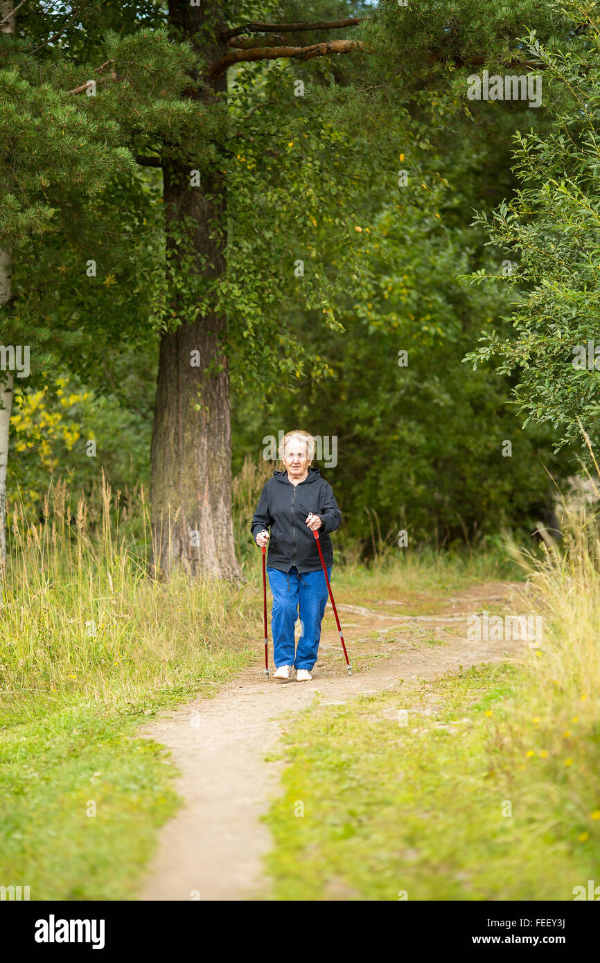 Una donna anziana in una passeggiata nel parco la pratica del Nordic walking. Foto Stock