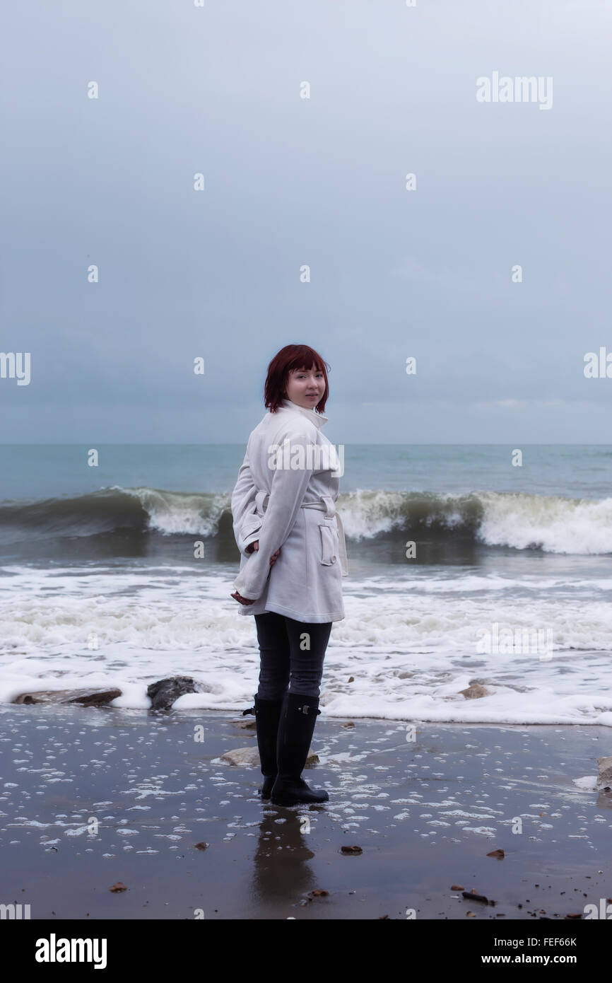 Una donna in camice bianco è in piedi al mare in inverno Foto Stock