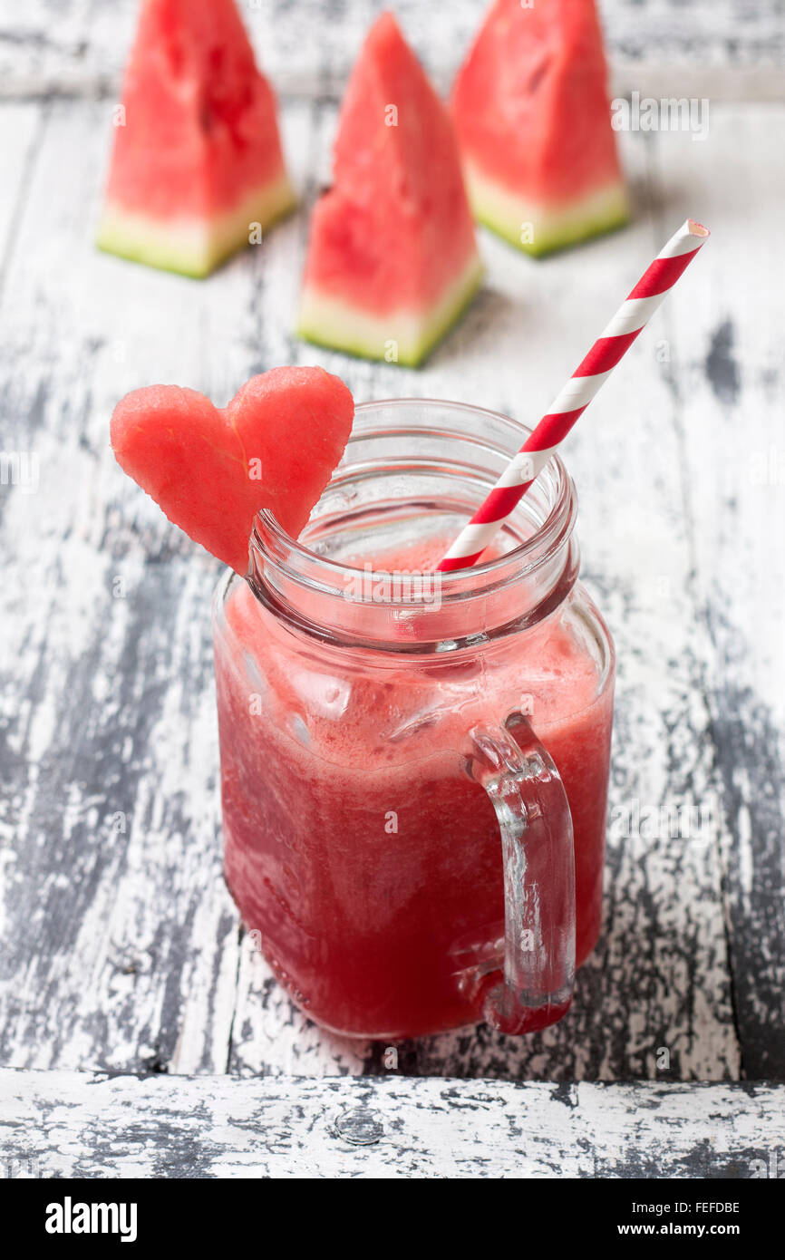 Fresco frullato di anguria in una giara di mason, fette di cocomero su uno sfondo di legno Foto Stock