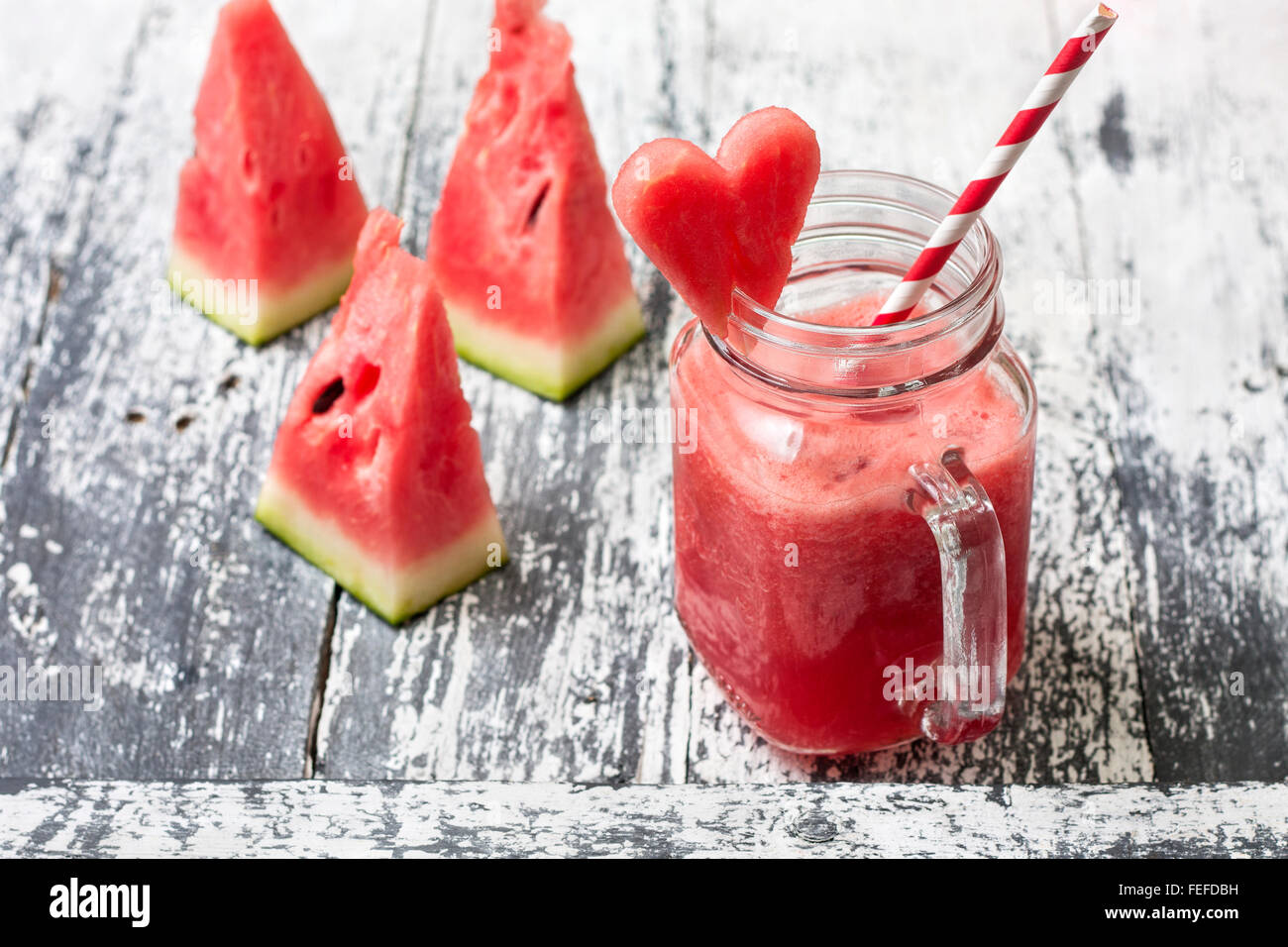 Fresco frullato di anguria in una giara di mason, fette di cocomero in forma di cuore sullo sfondo di legno Foto Stock