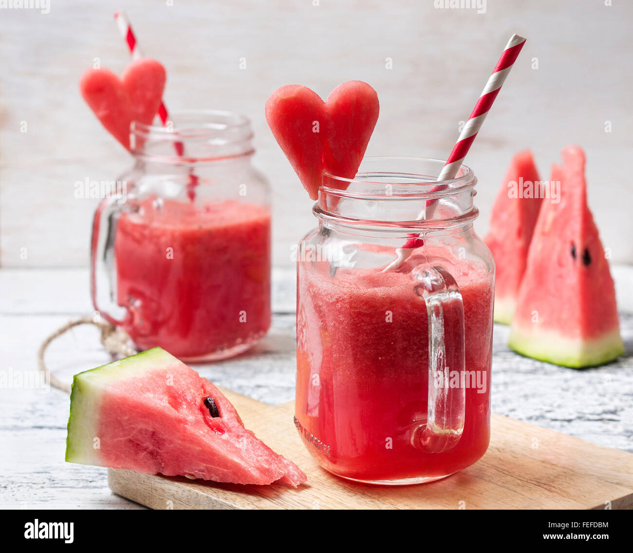 Fresco frullato di anguria in una giara di mason, fette di cocomero in forma di cuore sullo sfondo di legno Foto Stock