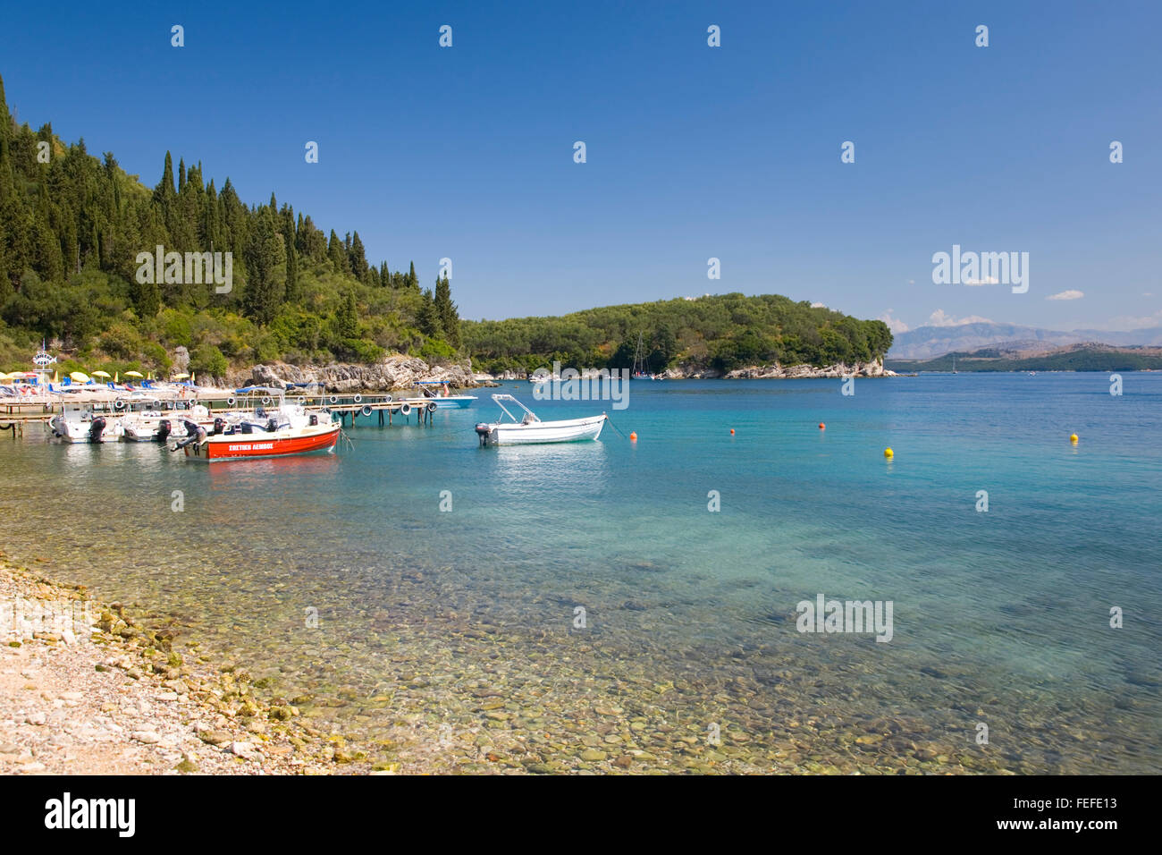 Kalami, Corfu, Isole Ionie, Grecia. Vista dalla riva attraverso le acque turchesi della baia Agni, piccole imbarcazioni al punto di ancoraggio. Foto Stock