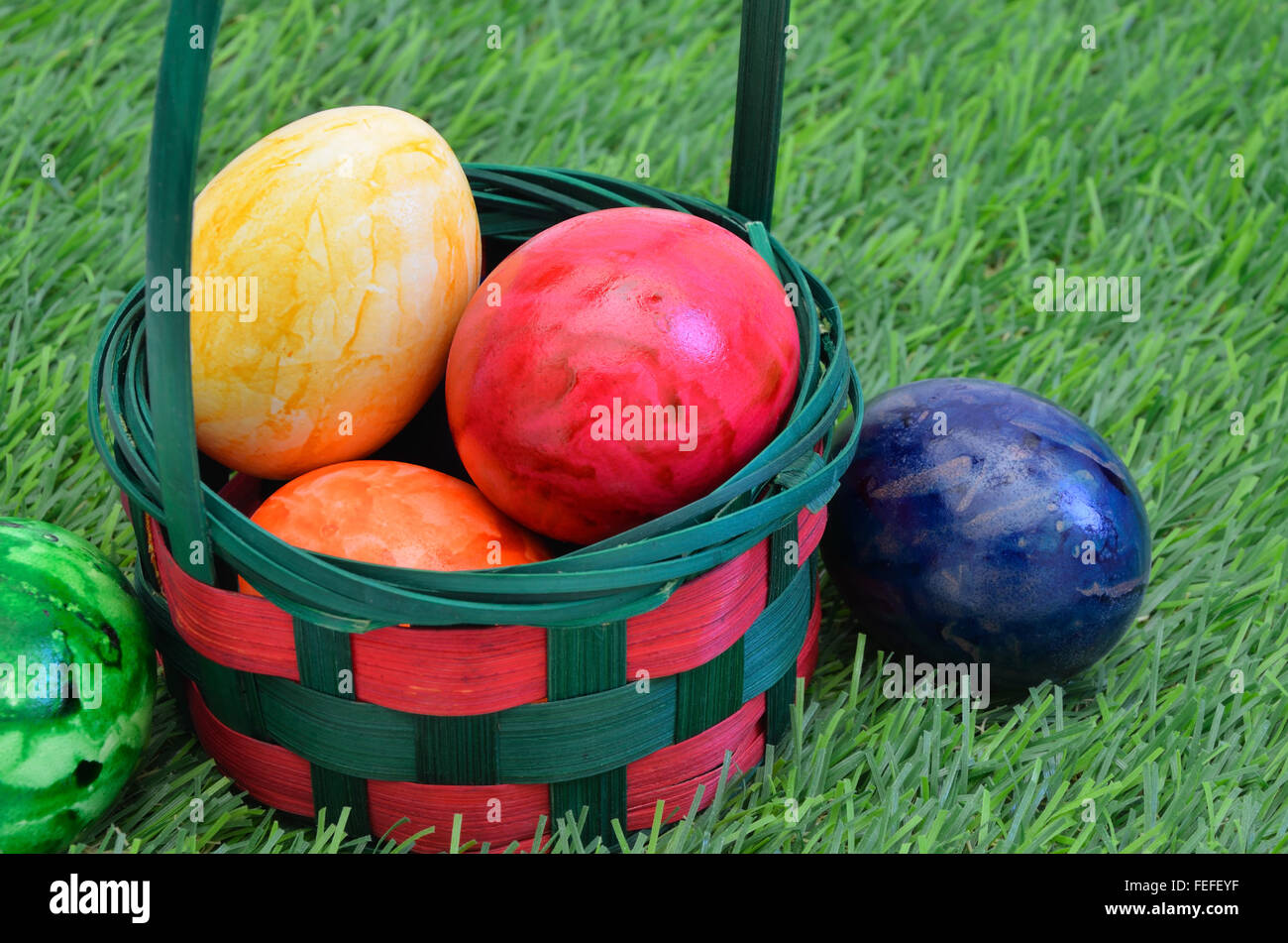 Colorate le uova di Pasqua in un paniere esterno su erba verde, vicino, full frame, orizzontale Foto Stock