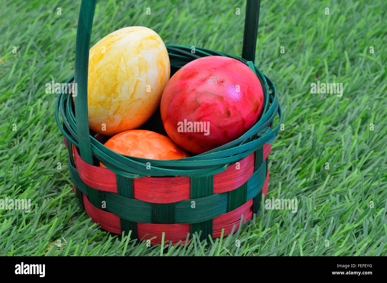 Colorate le uova di Pasqua in un paniere esterno su erba verde, vicino, full frame, orizzontale Foto Stock