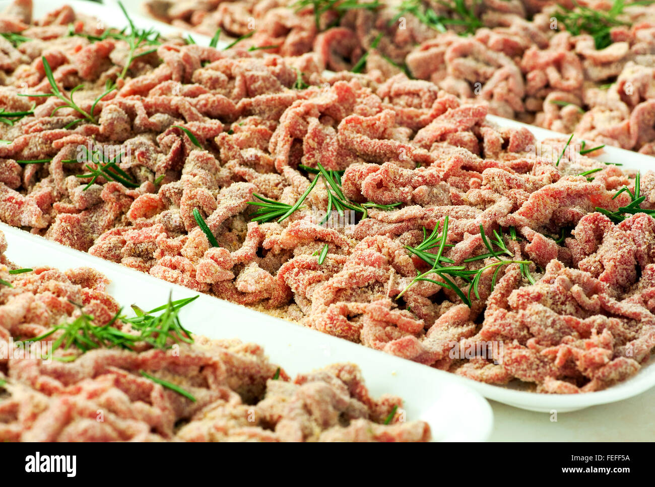 Vassoi di impanati o impanati strisce di carne di manzo crudo guarnito con rosmarino fresco sul display in una macelleria per la vendita Foto Stock