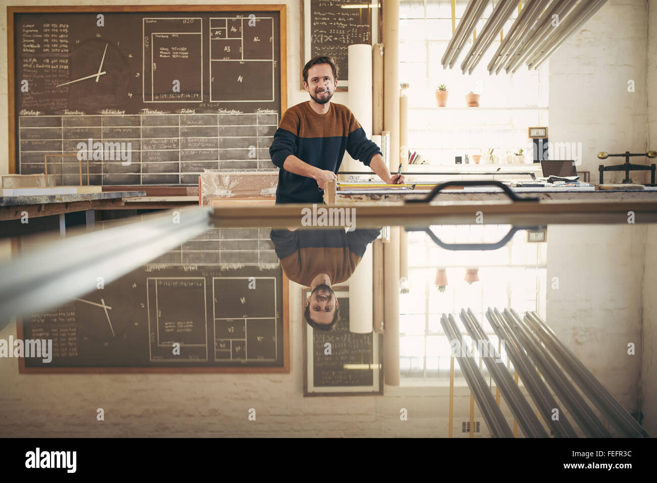 Ritratto di un positivo e professional framer al lavoro nel suo studio, con strumenti sul suo banco e guardando verso l'alto la fotocamera w Foto Stock