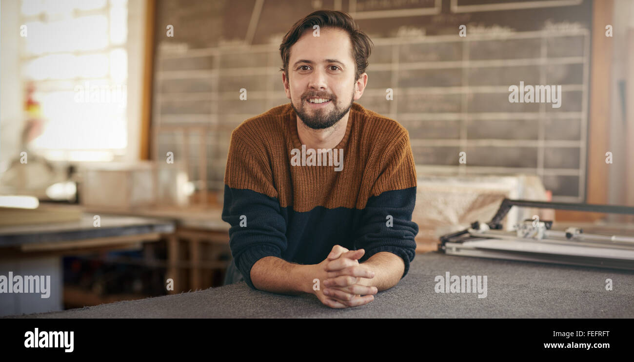 I giovani designer di sesso maschile con un espressione positiva appoggiata casualmente su di un area di lavoro nel suo studio Foto Stock