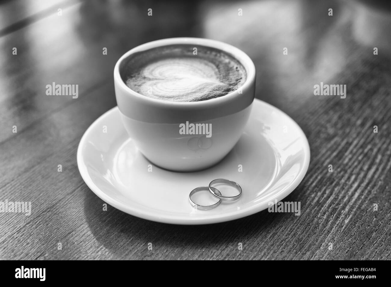 Gli anelli di nozze e la tazza di caffè con la schiuma a forma di cuore Foto Stock