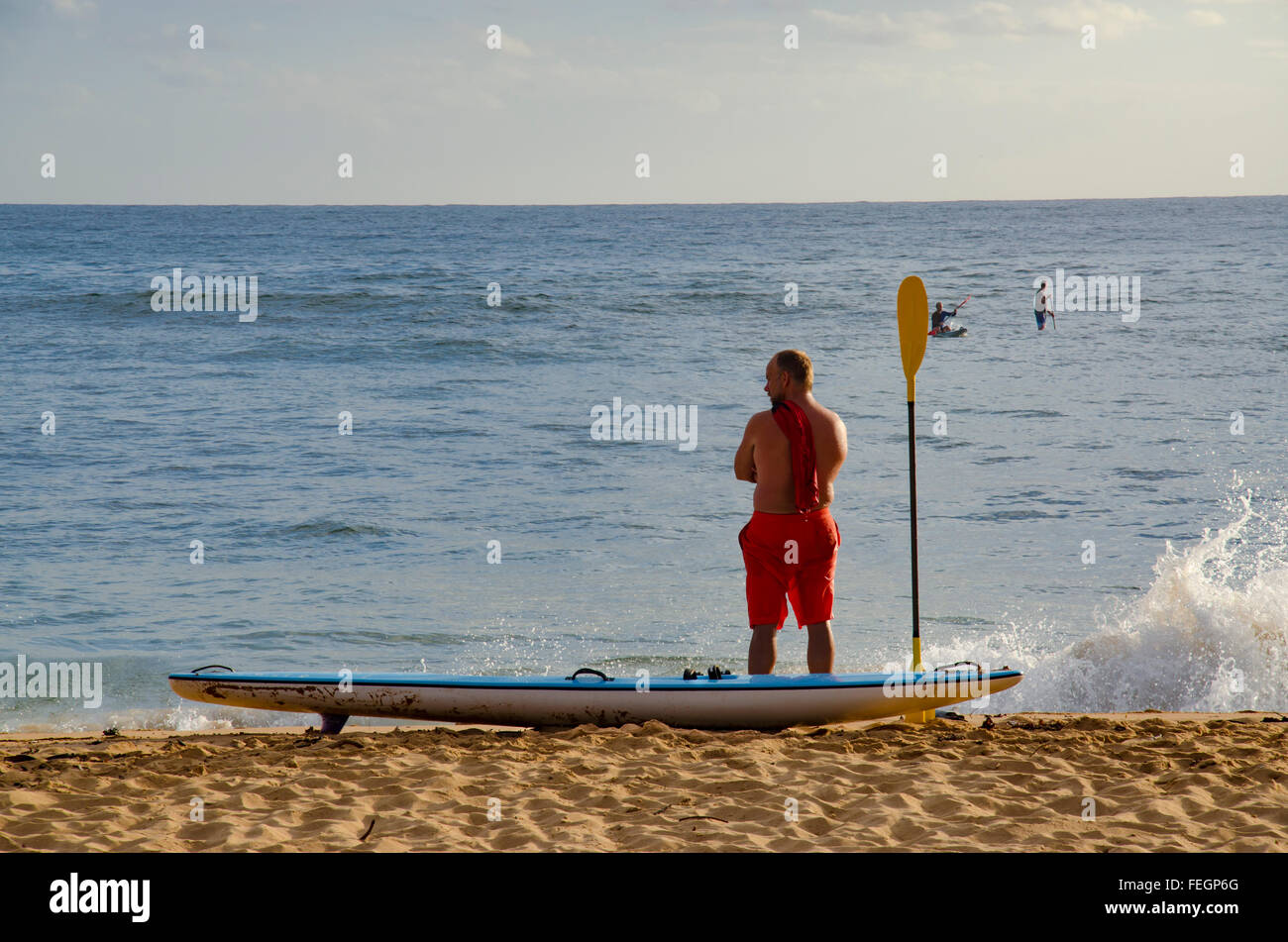 Un pilota di surf da sci si erge sul litorale di Collaroy Beach a Sydney nei suoi shorts da surf che guardano sull'acqua Foto Stock