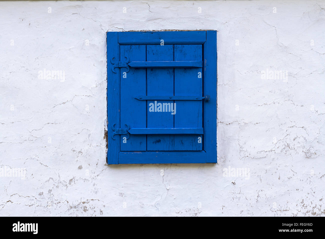 Orizzontale vista frontale di una finestra blu con chiusura ciechi di legno su un bianco edificio a trama parete Foto Stock